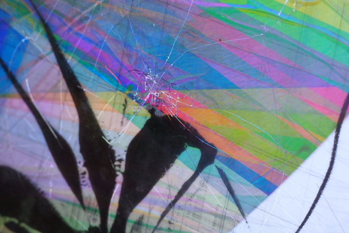 Close-up of a computer screen with a spiderweb pattern of cracks overlaying a colorful digital glitch art background.