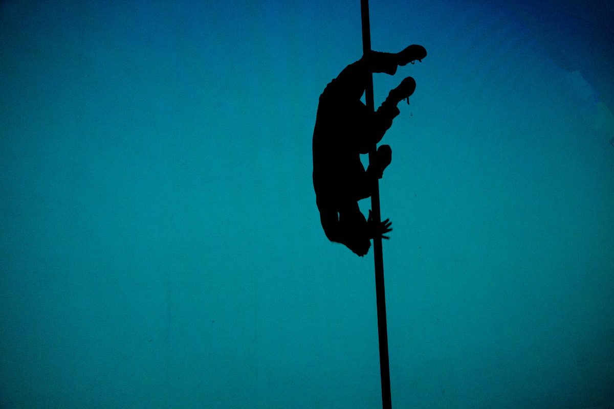 Silhouette of a Chinese pole artist performing a dynamic pose against a monochrome blue background.
