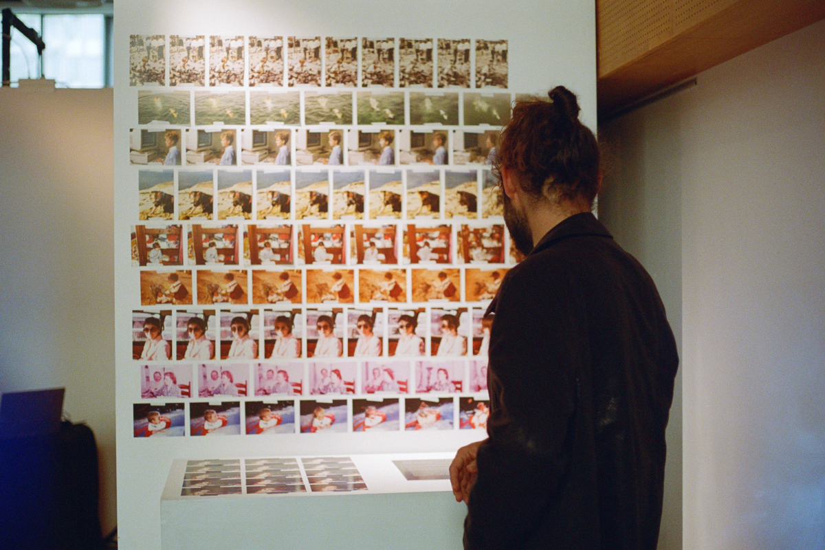 A person is observing a wall display of repeated family photographs at an exhibition